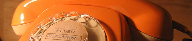 Das Bild zeigt die Detailaufnahme der Wählscheibe eines orangefarbenen Telefons. In der Mitte der Wählscheibe ist die Rufnummer der Geschäftsstelle des Vereins zu sehen