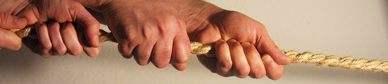 Das Bild zeigt die Detailaufnahme zweier Händepaare, die gemeinsam an einem dicken Seil ziehen. Das Seil ist gespannt
